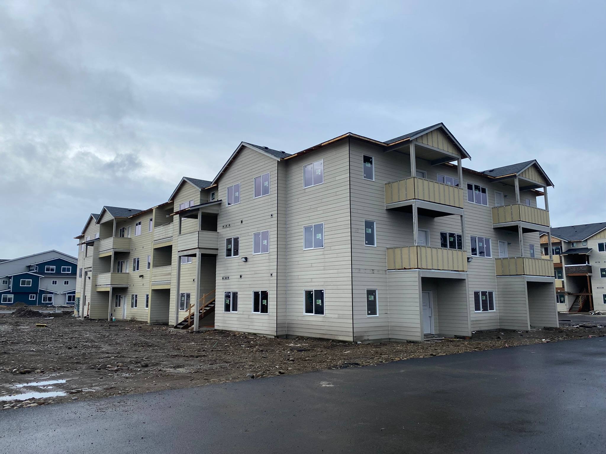Three-story apartment building with light lap siding, white trim, and stacked balconies