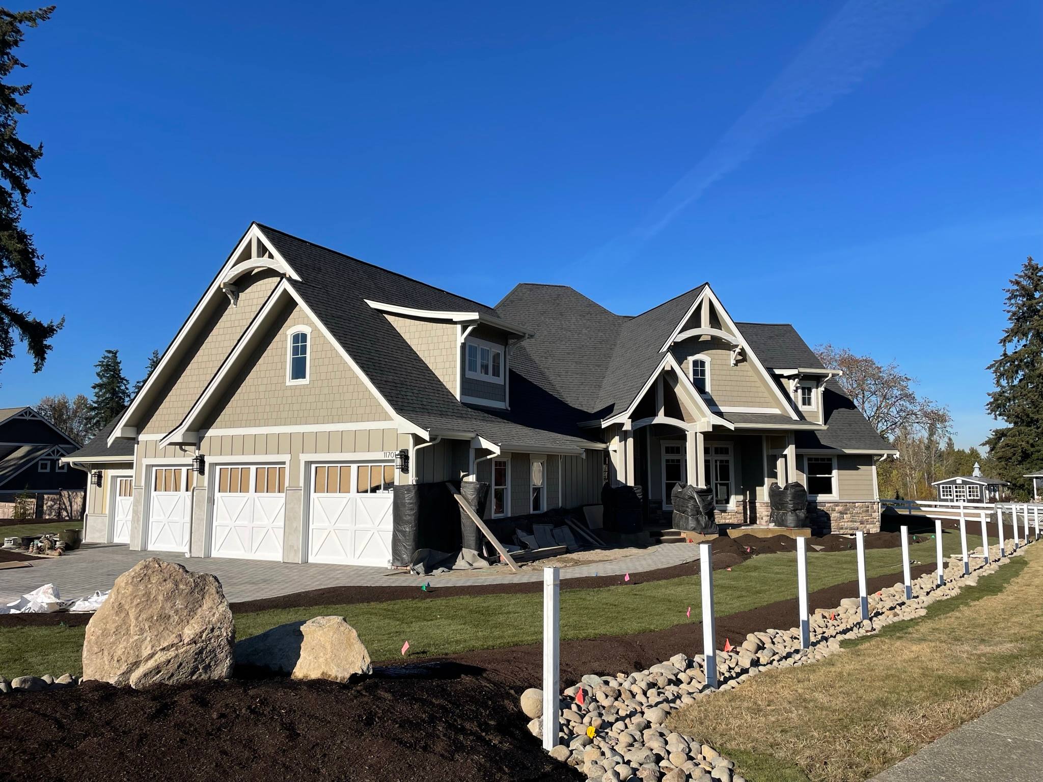 Large craftsman-style home with tan board and batten siding, shake gables, white trim, and three carriage-style garage doors