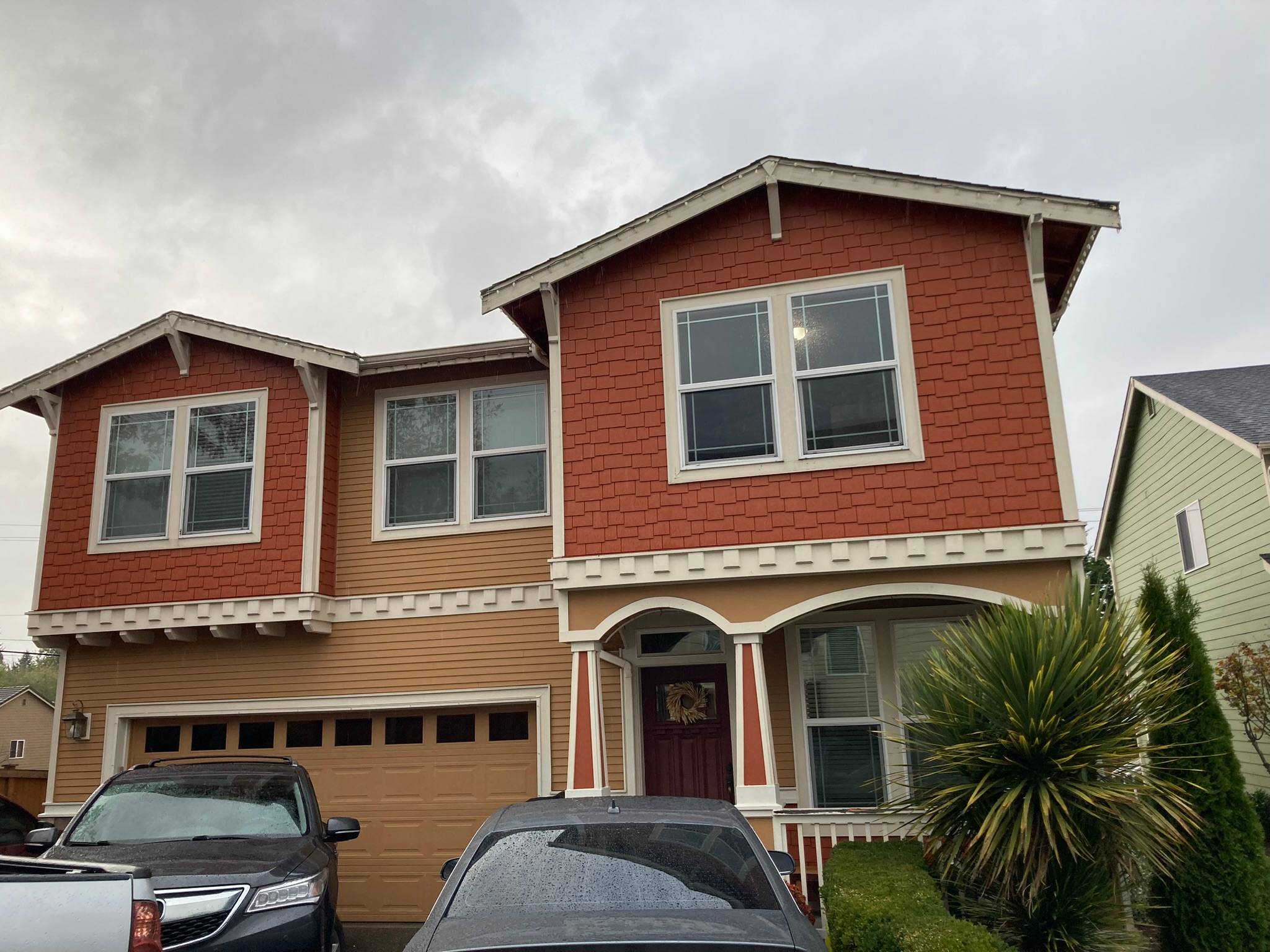 Two-story home with red shingle siding upstairs, tan lap siding below, and white trim
