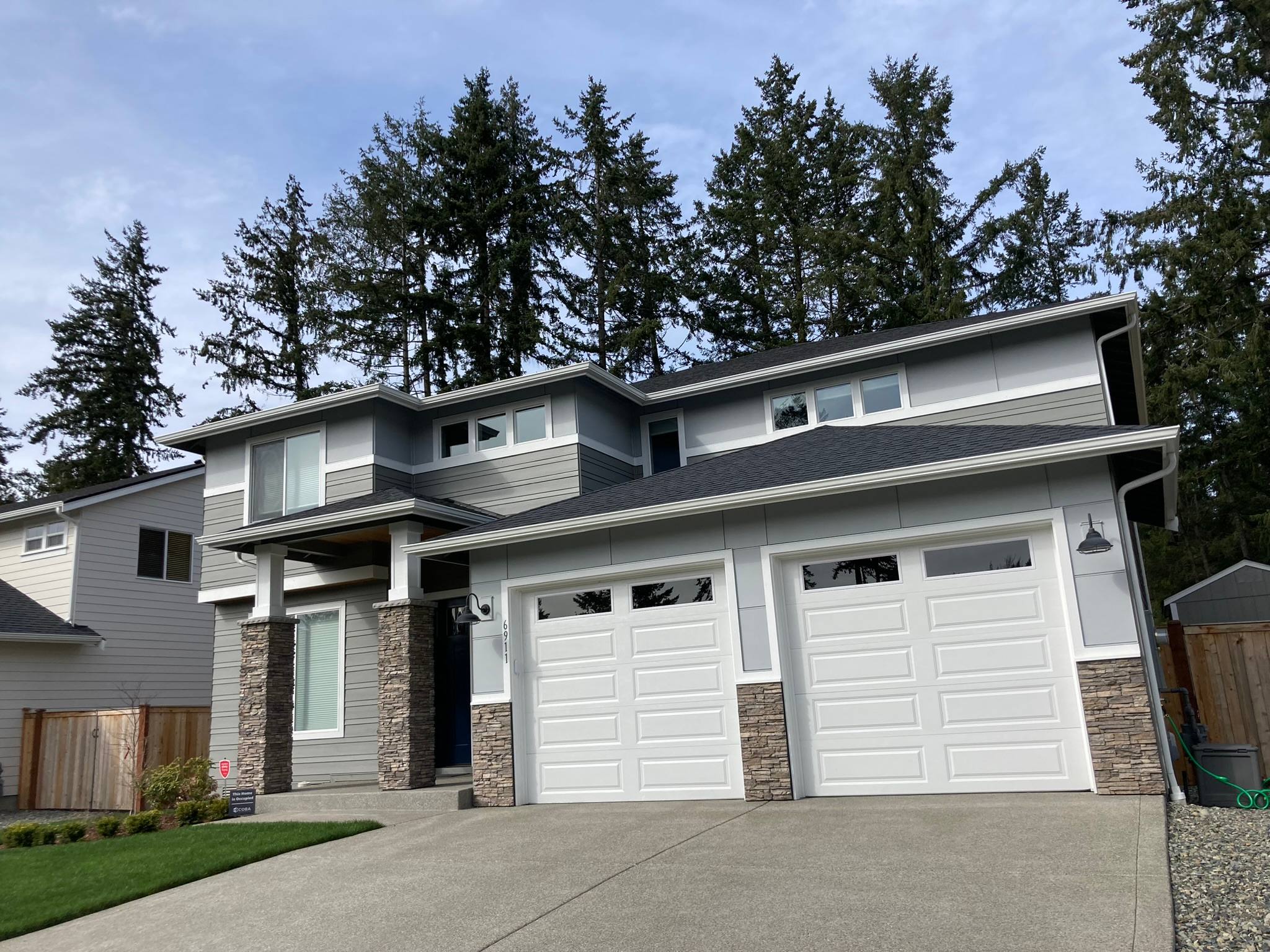 Two-story gray home with lap siding, board and batten accents, stone columns, and a two-car garage