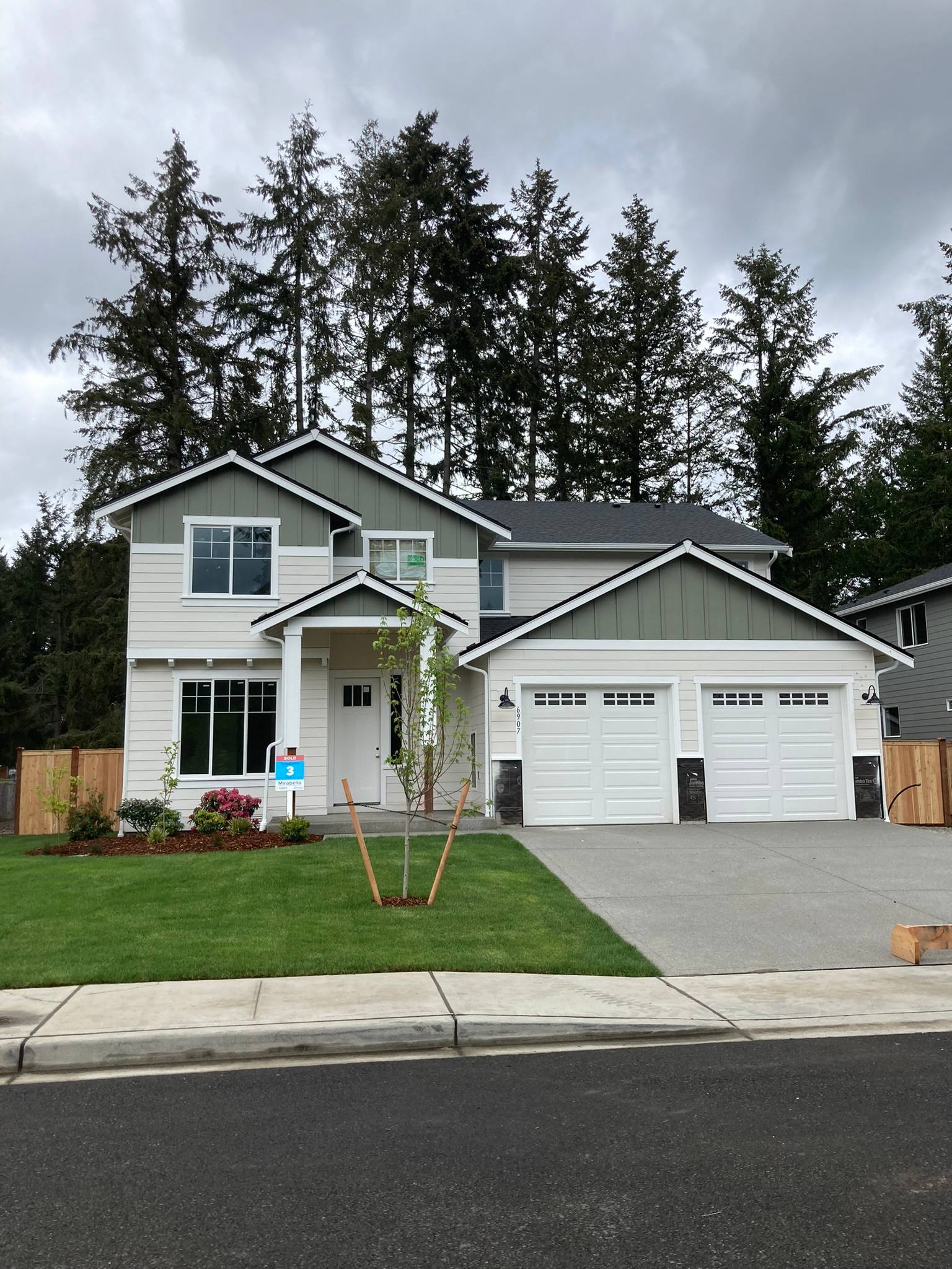 Two-story home with light gray lap siding and a sage green board and batten gable over the entry
